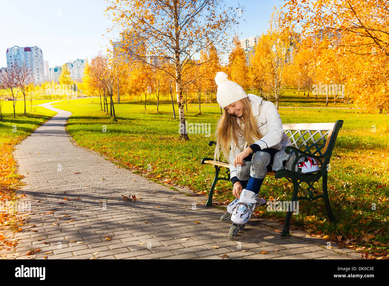 Blonde Teen Mädchen mit langen Haaren im Herbst Park auf der Bank sitzen und setzen auf Rollerblades Stockfoto