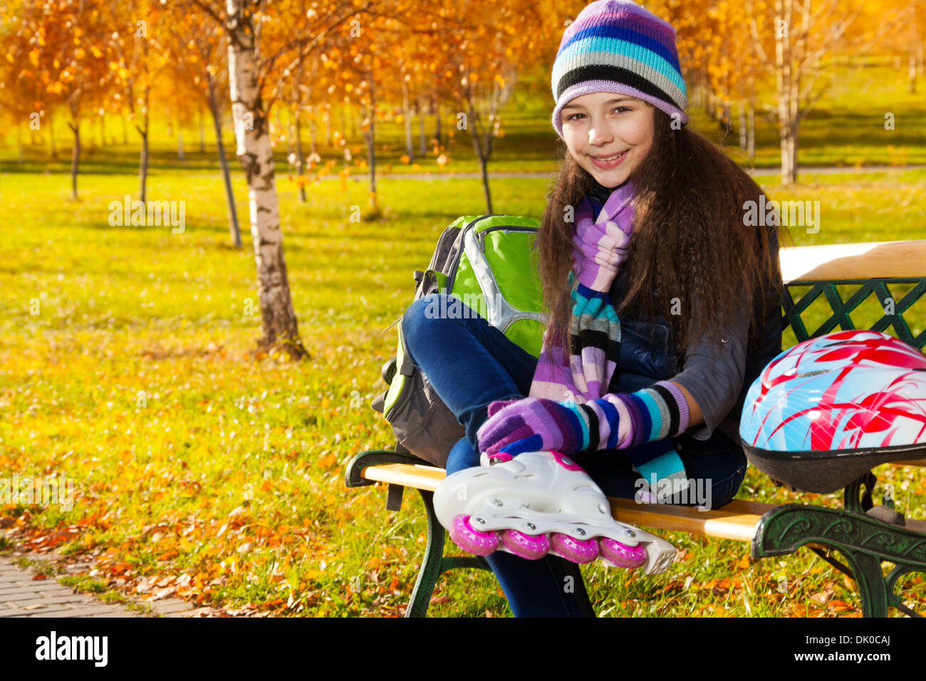 Schließen Portrait von wunderschönen 11 Jahre altes Mädchen setzen auf roller blades in warme Kleidung im Park auf der Bank sitzen im Herbst park mit Helm auf der Werkbank Stockfoto