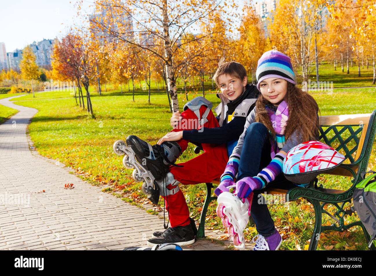 Kinder setzen auf rollschuhe 10 und 11 Jahre alte Paar Schule Kinder, Junge ein Mädchen in der warmen Herbst Kleidung auf der Bank im Park Stockfoto