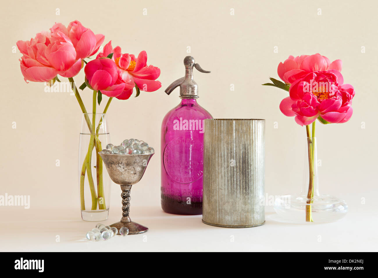 Stillleben mit rosa Pfingstrosen in Vasen neben Selters Flasche und Silber-Container Stockfoto