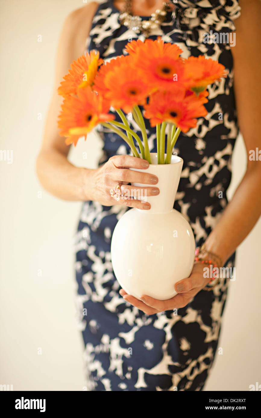 Mittelteil Porträt der Frau im Kleid mit orange Gerber Daisies in vase Stockfoto