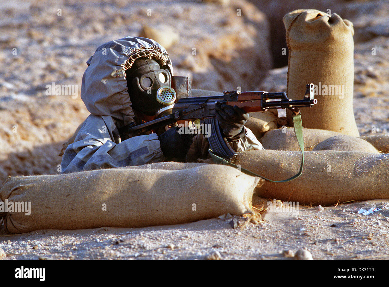 Ein syrischer Soldat soll ein AK-47 Sturmgewehr aus seiner Position in einem Erdloch während einer Feuerkraft Demonstrationsteil der Operation Desert Shield 14. Februar 1991 in Saudi Arabien. Der Soldat trägt ein sowjetischer Modell ShMS-nuklearen-biologisch-chemische Kriegsführung-Masken. Stockfoto