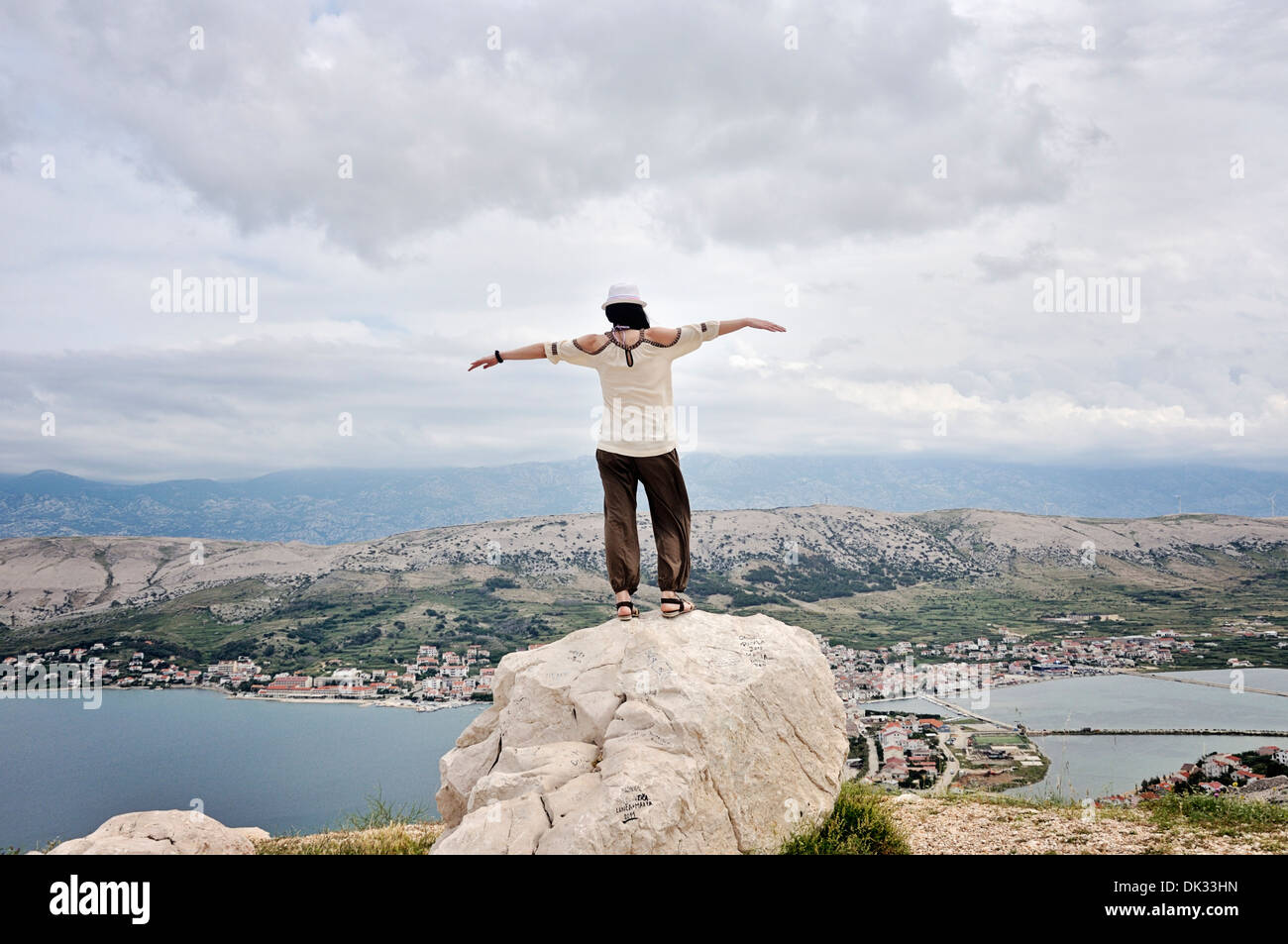 Mitte Erwachsene Frau mit ausgestreckten Armen auf Felsen mit Blick auf die Stadt Pag, Insel Pag, Kroatien, Europa Stockfoto