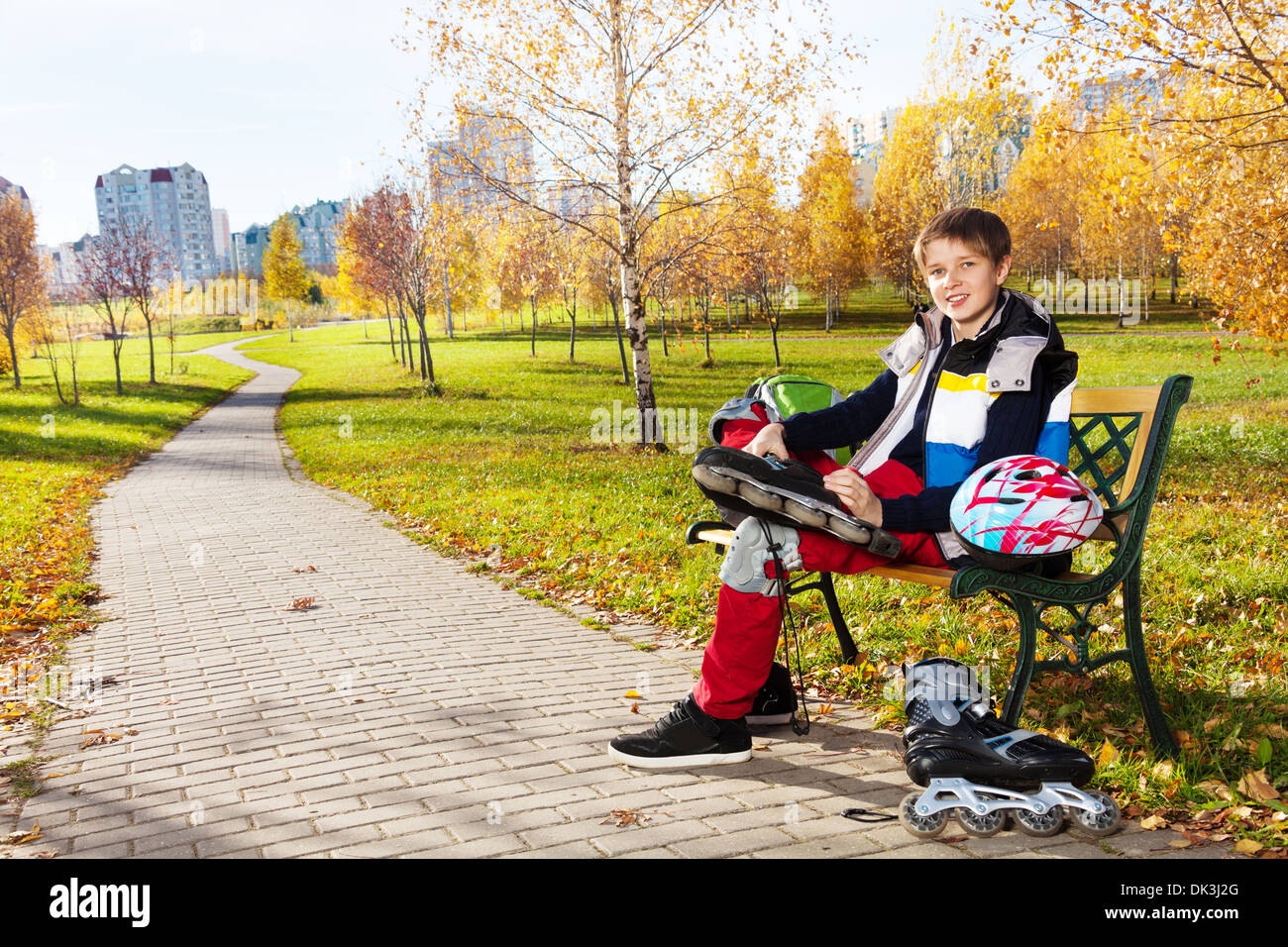 Glücklich lächelnd 10 Jahre alter Junge sitzt auf der Bank im herbstlichen Park und setzen auf Rollerblades Stockfoto