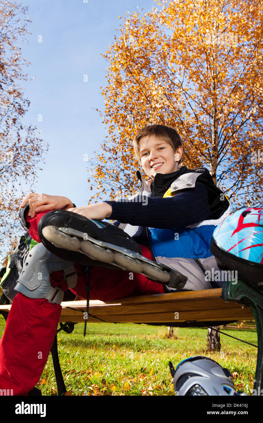 10 Jahre alter Junge sitzt auf der Bank im Herbst Park mit Rollerblades aus niedrigen Winkel schießen Stockfoto