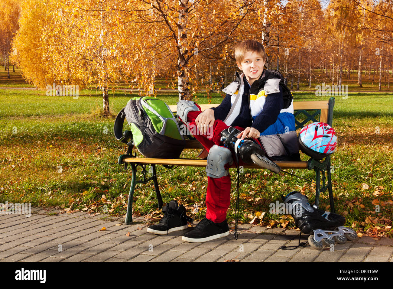 10 Jahre alten Schuljunge sitzt auf der Bank im Herbst Park mit Rollerblades Stockfoto