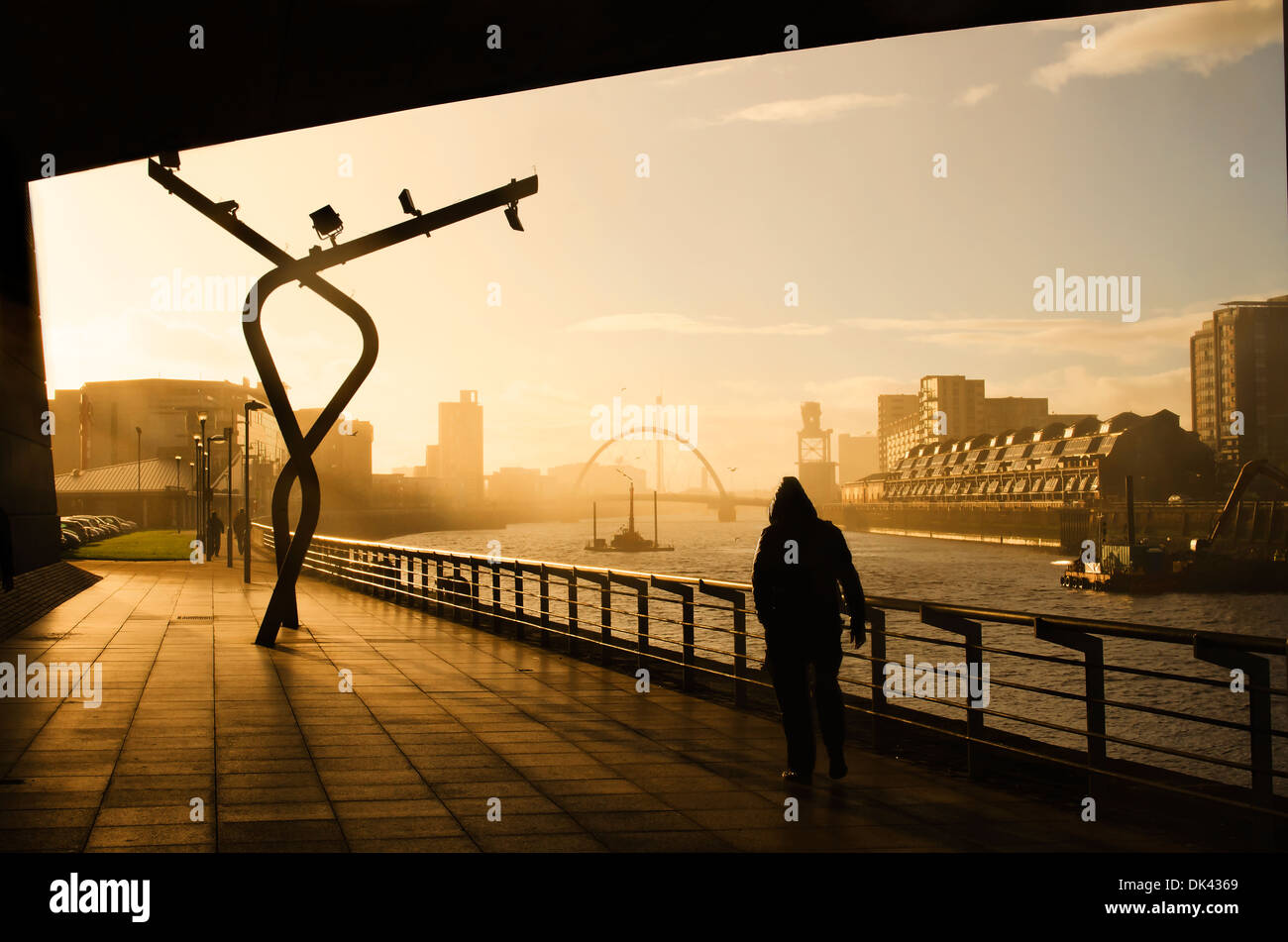 Ein Mann geht unter einer Brücke in Glasgow während eines Regenschauers, wie die Sonne beginnt sich hinter der Wolke Stockfoto