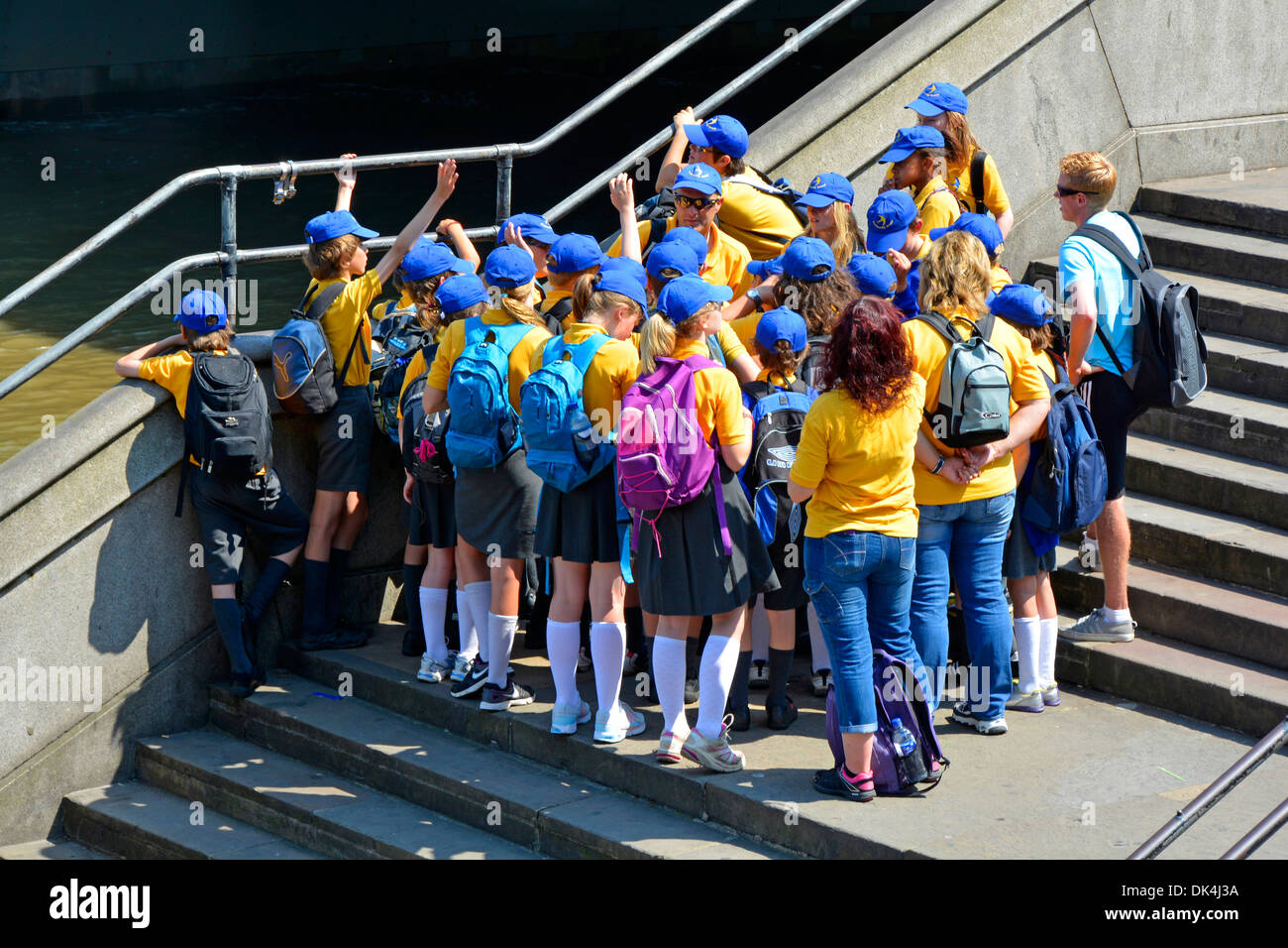 Kinder in blauen Mützen und farbenfrohen Schuluniformen für Jungen und Mädchen mit Lehrern, die an der Themse in Westminster London, England, teilhaben Stockfoto