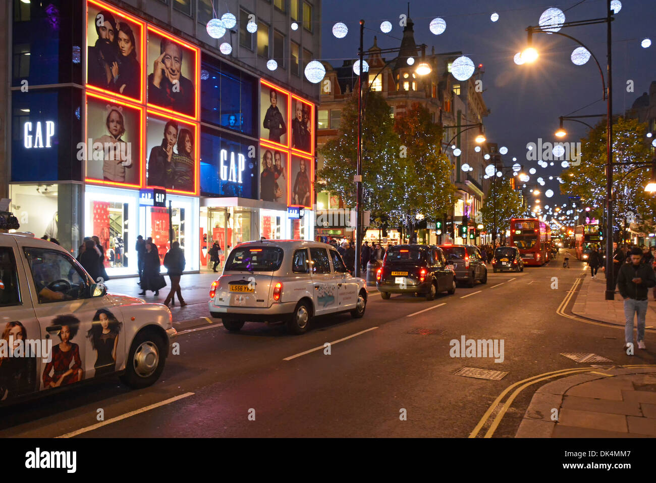 Oxford Street West End of London Taxis stehen in der Shopping Street Szene vor Gap Bekleidungsgeschäft Nacht beleuchtete Weihnachtsdekoration England Großbritannien Stockfoto
