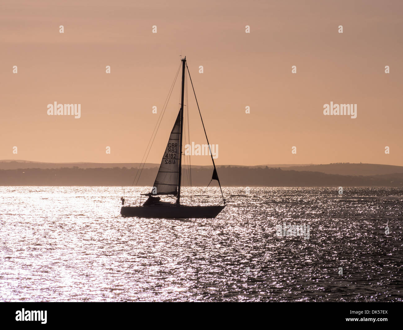 Silhouette einer Yacht auf dem Solent am Abend mit der Isle Of Wight im Hintergrund Stockfoto