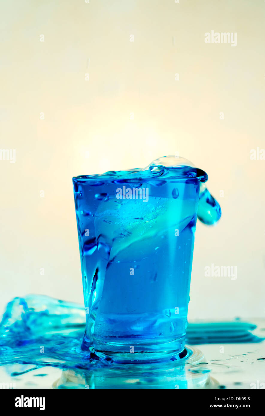 Glas mit blauem Wasser verschütten hinunter die Seiten Stockfoto