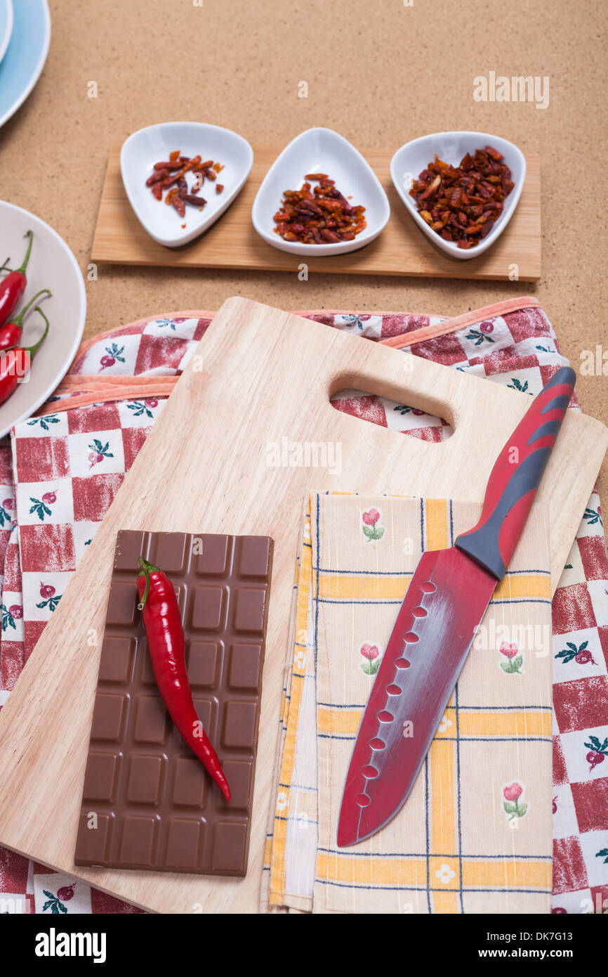 Rote Chilischoten mit Schokolade und Messer auf Schneidebrett. Stockfoto