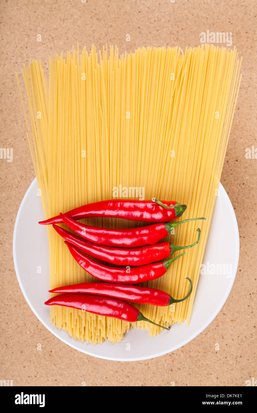 Teller mit frischen Chili-Paprika und getrockneten Teigwaren über hölzerne Hintergrund. Stockfoto