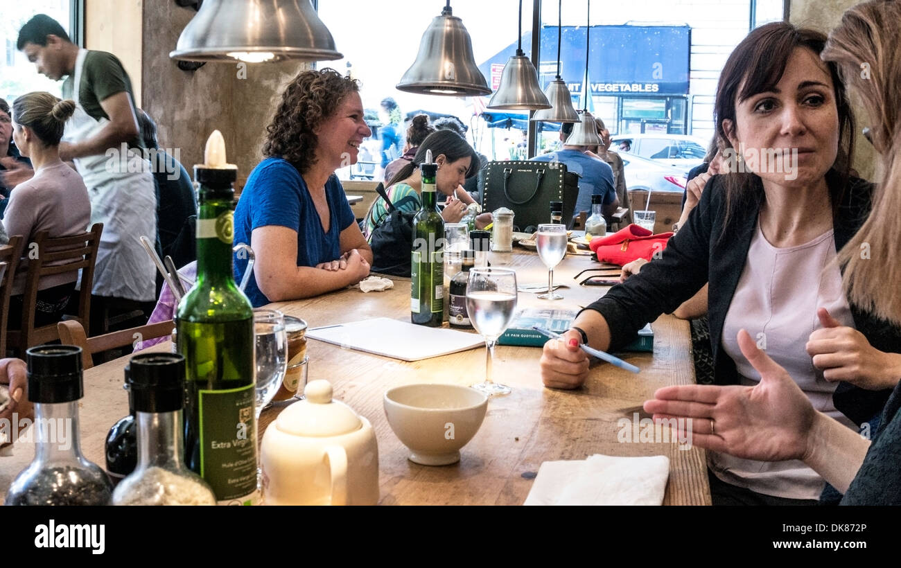 Gäste genießen angeregten Gespräch am gemeinsamen Tisch in geselliger Atmosphäre des trendigen Le Pain Quotidien in Midtown Manhattan Stockfoto