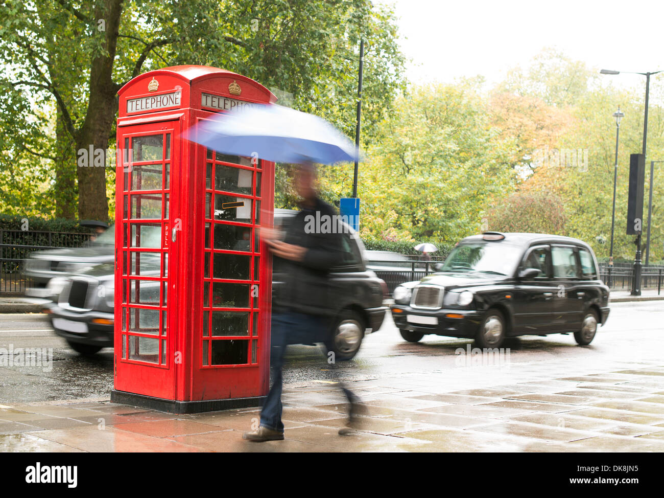 Rote Telefon Kabine in London. Mann mit Regenschirm Stockfoto