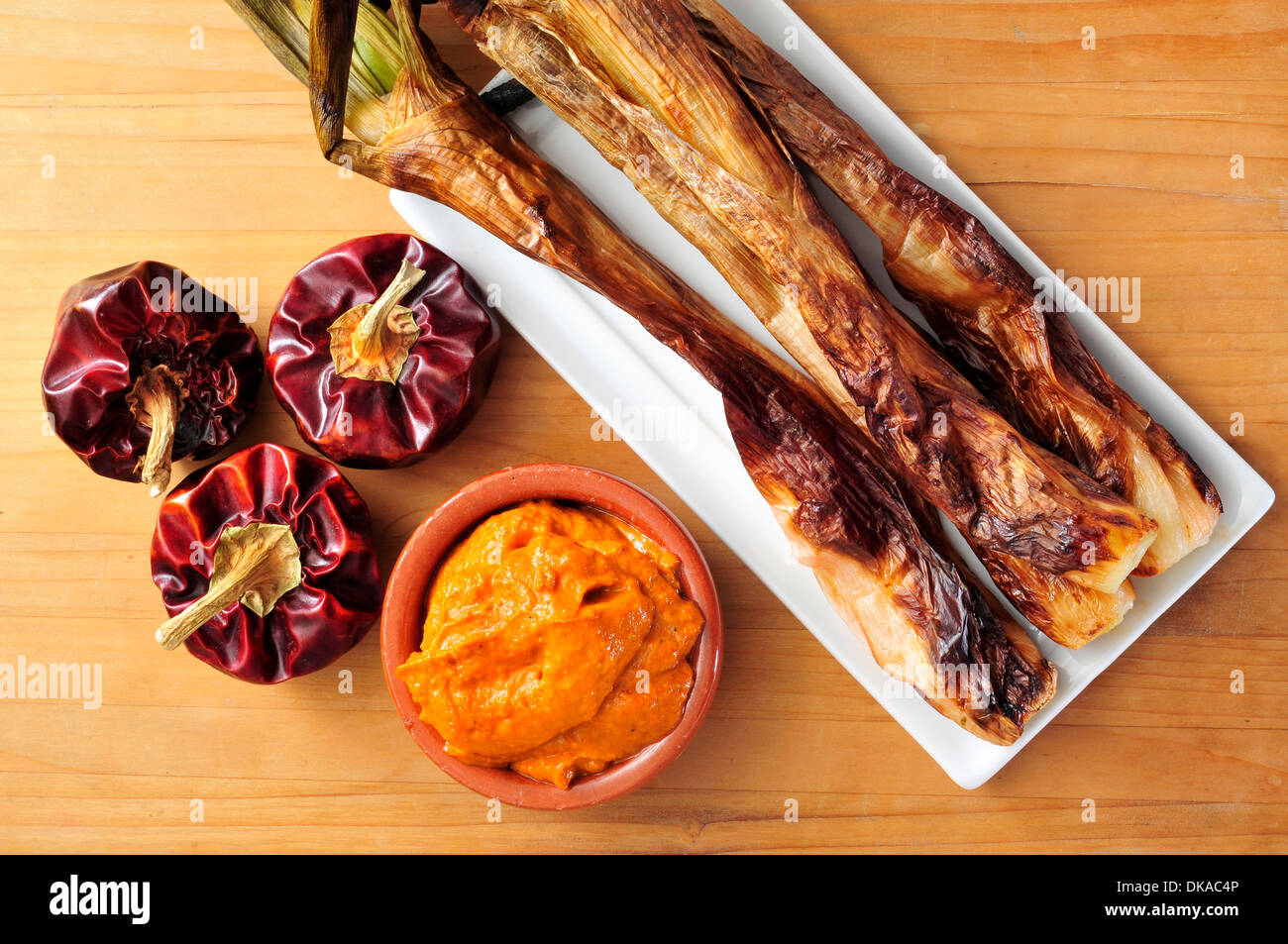 Nahaufnahme einer Platte mit gegrilltem Calcots, süße Zwiebeln und eine Schüssel mit Romesco-Sauce, typisch für Katalonien, Spanien Stockfoto