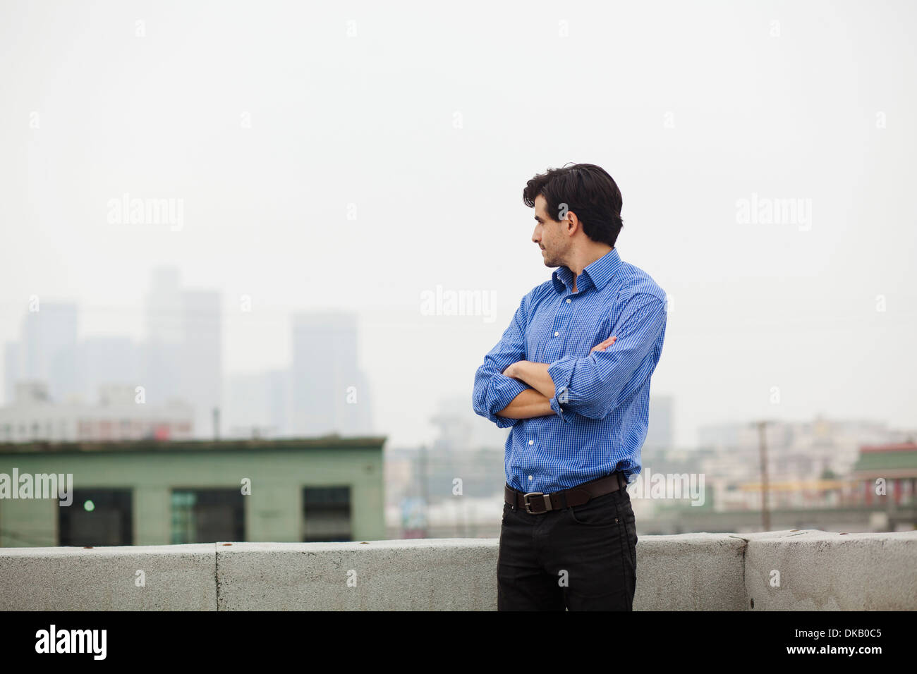 Junger Geschäftsmann mit verschränkten Armen auf Stadt auf dem Dach Stockfoto