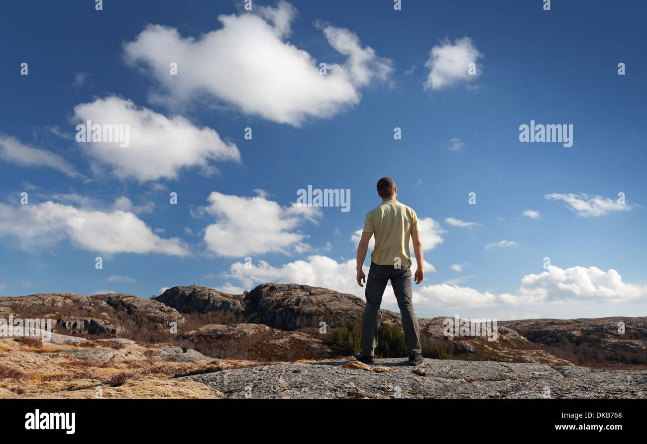 Junger Mann starrte auf blauen Himmel steht auf felsigem Boden Stockfoto