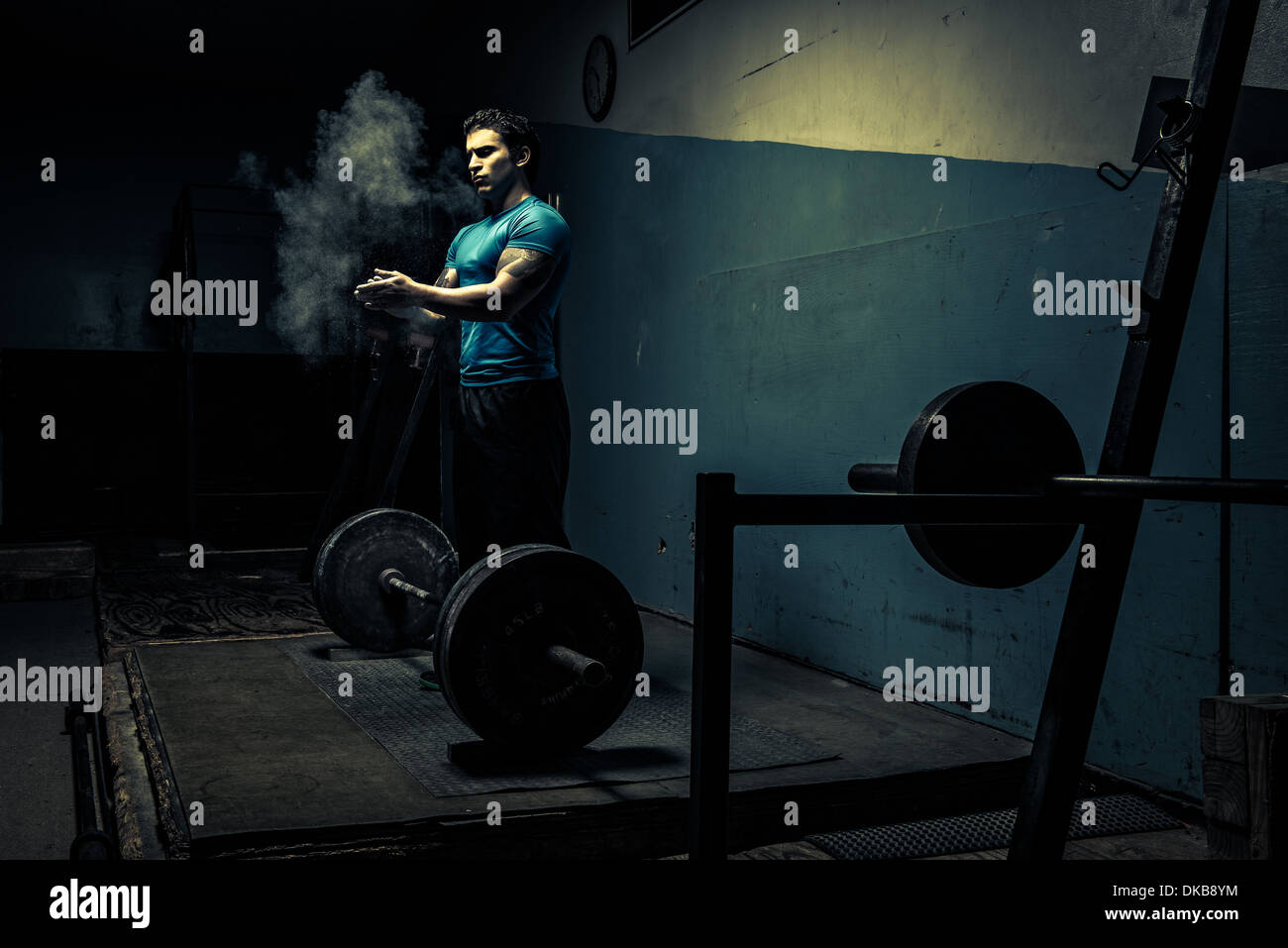 Gewichtheber in dunklen Turnhalle, indem Kreide auf Händen Stockfoto