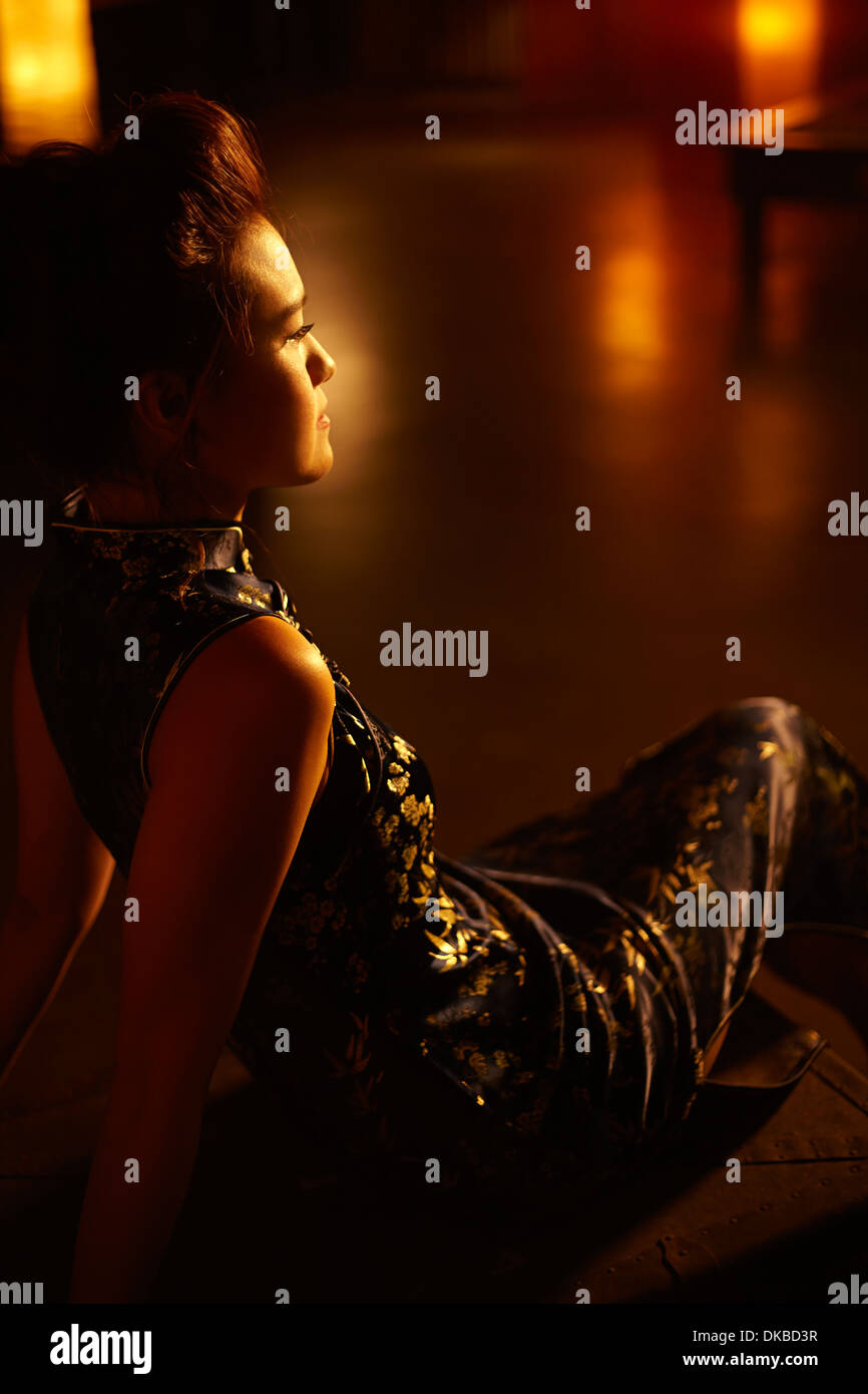 Junge Frau sitzt im abgedunkelten Raum Stockfoto