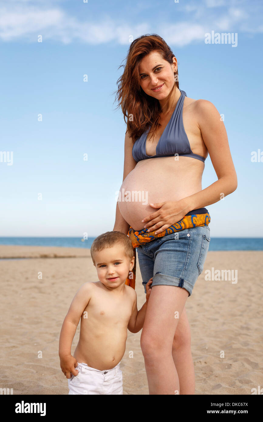 Schwangere Frau am Strand, hand auf Bauch, mit Kleinkind Stockfoto