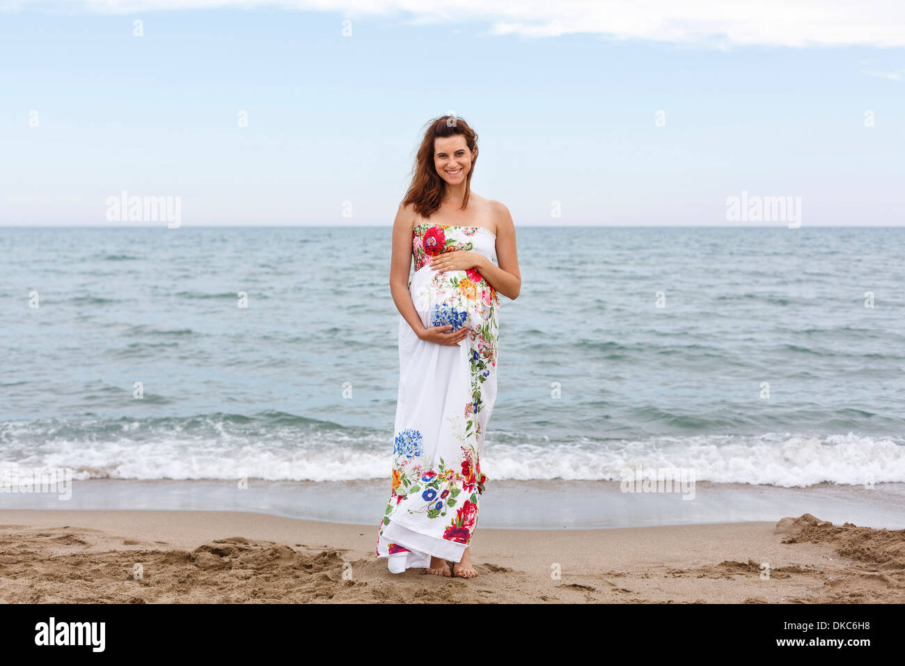 Schwangere Frau stehen am Strand, die Hände auf Bauch Stockfoto
