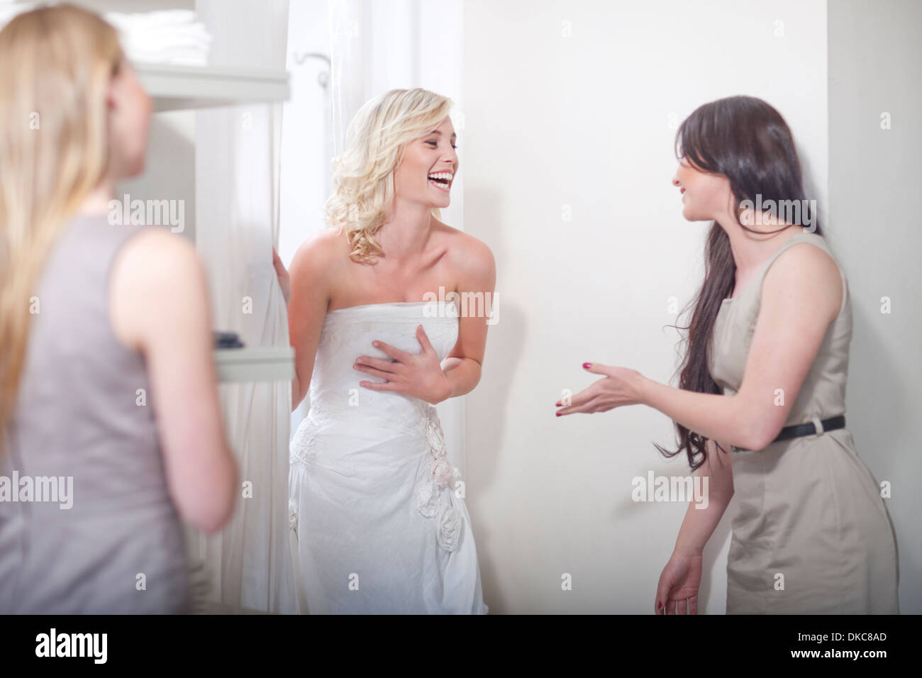 Junge Frau, die versucht auf Hochzeitskleid, mit Freunden Stockfoto