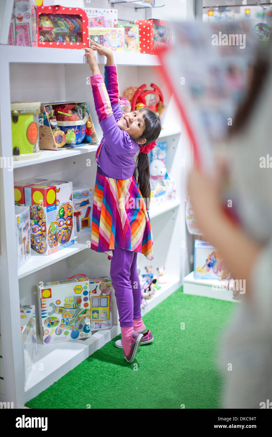 Junges Mädchen Strecken sich auf Zehenspitzen im Spielzeugladen Stockfoto