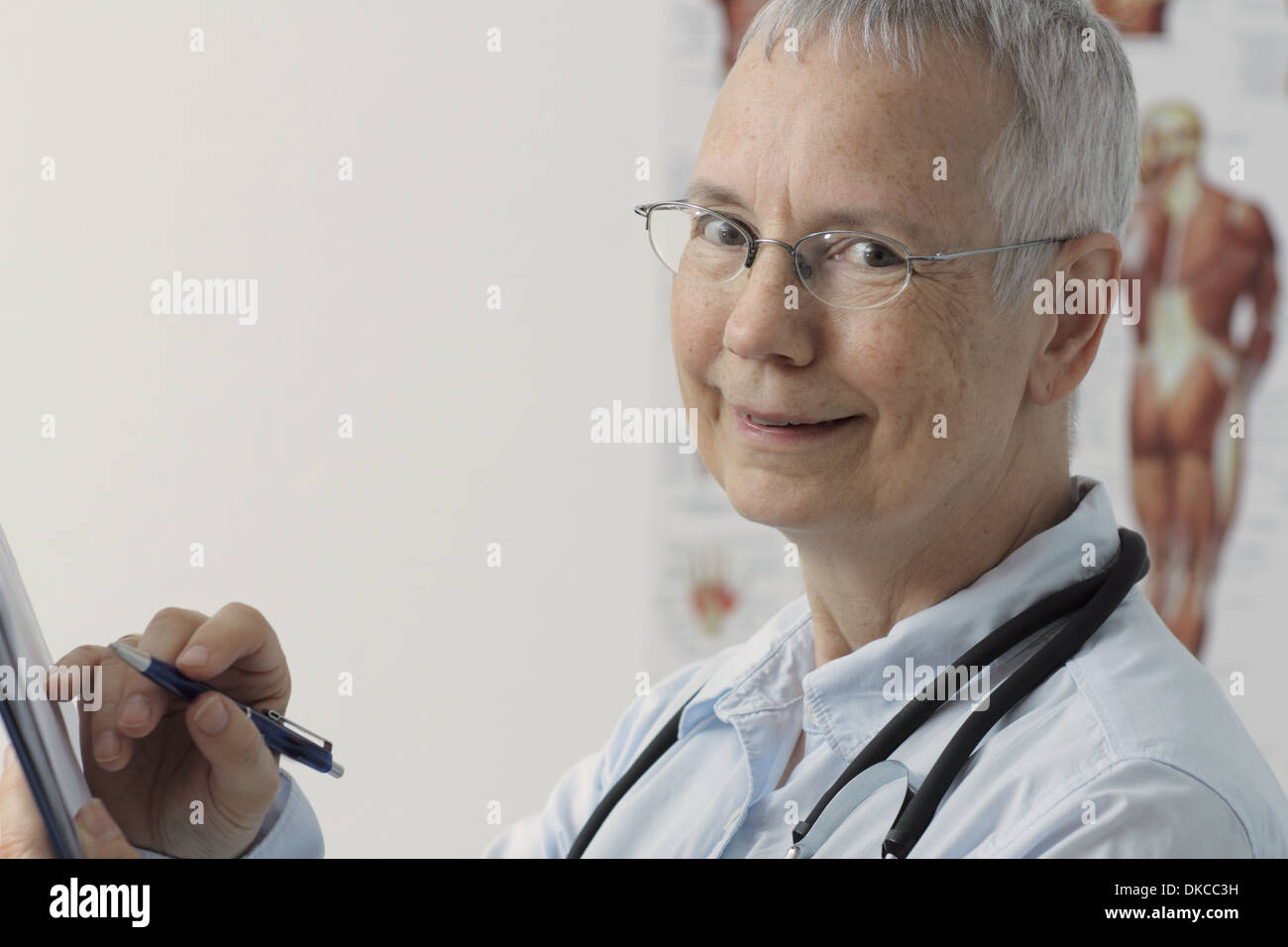 eine lachende Frau Doc mit einem menschlichen Muskel Person Plakat im Hintergrund und mit einem Stift auf Laptop oder desktop Stockfoto