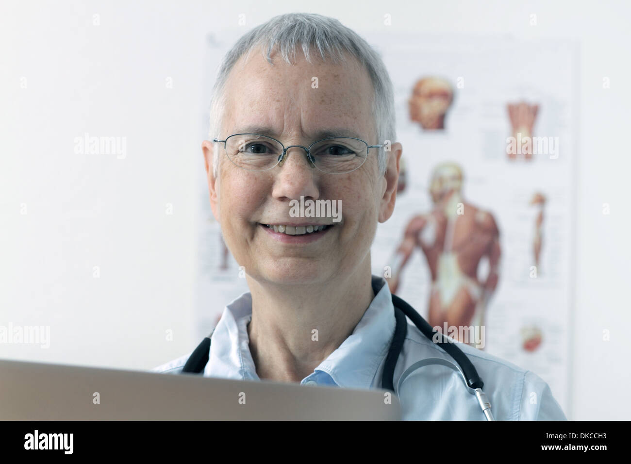 eine lachende Frau Doc mit einem menschlichen Muskel Person Plakat im Hintergrund und einem laptop Stockfoto