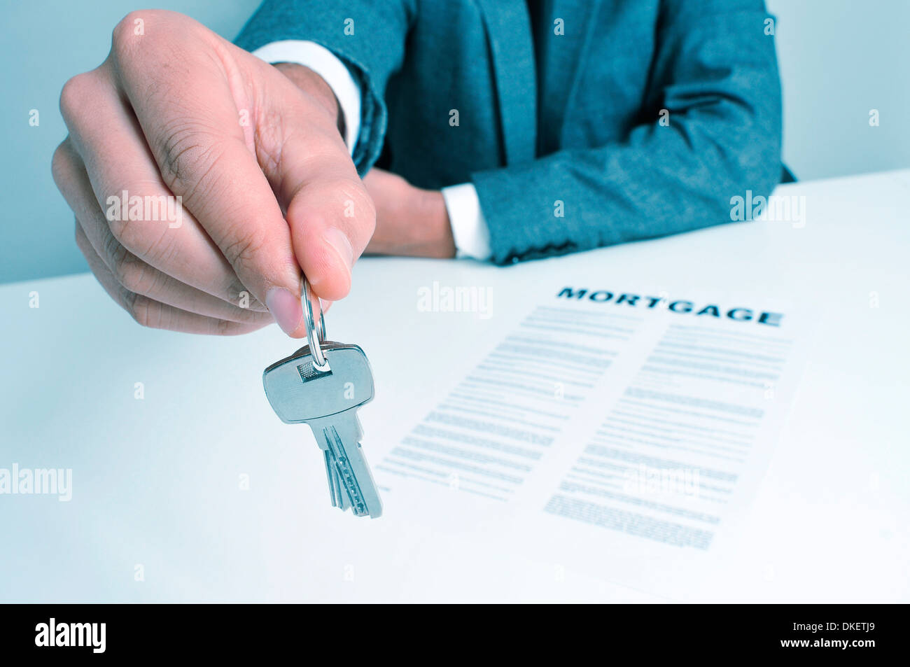 ein Mann in einem Anzug sitzt in einem Schreibtisch mit einer Hypothekenvertrag geben einen Schlüsselanhänger für dem Betrachter Stockfoto