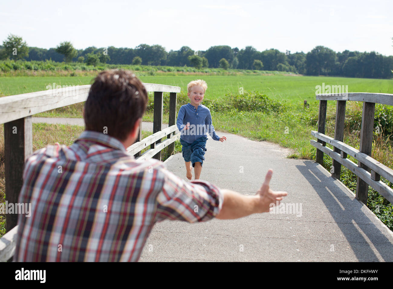 Junge, die hölzerne Brücke in Richtung Vater überfahren Stockfoto
