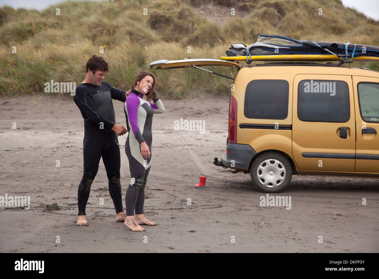 Mann hilft Frau anziehen Neoprenanzug am Strand Stockfoto