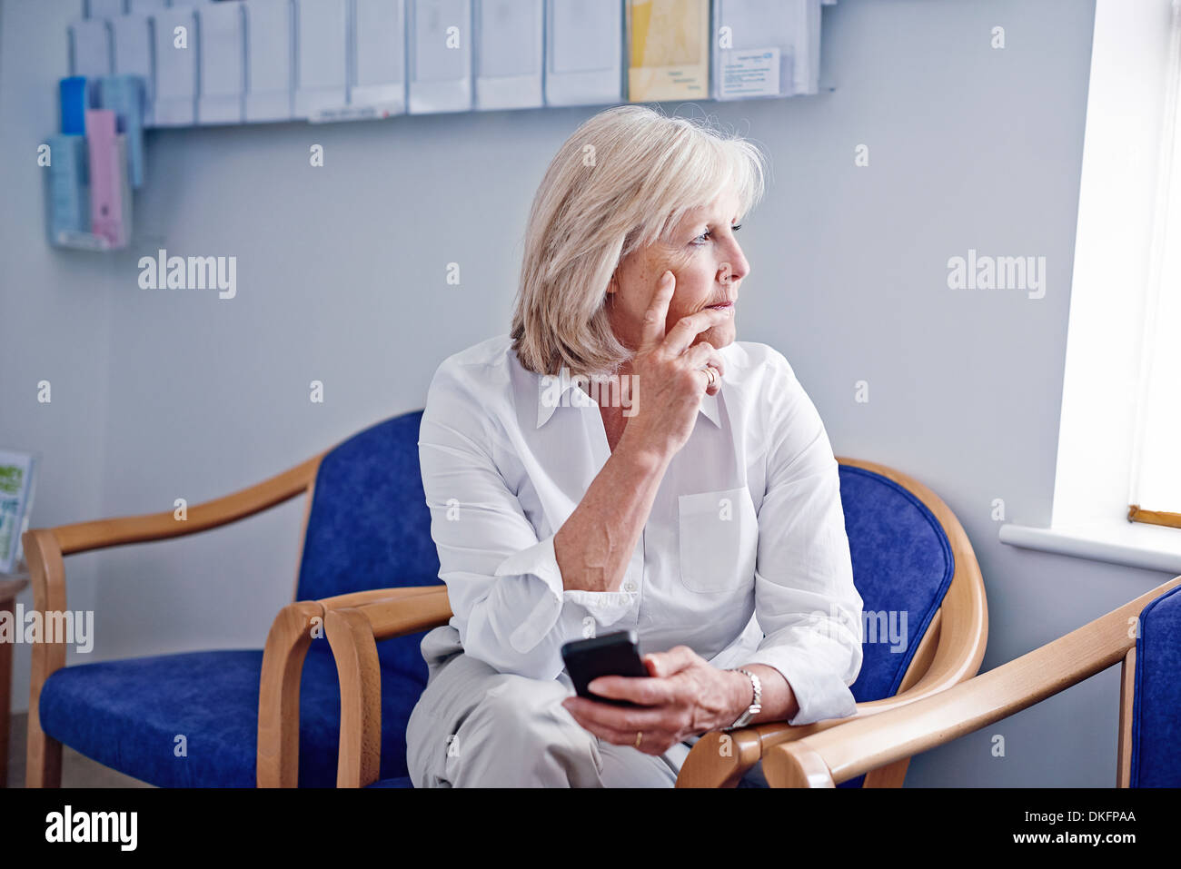 Ältere Patientin mit Handy im Krankenhaus Wartezimmer Stockfoto