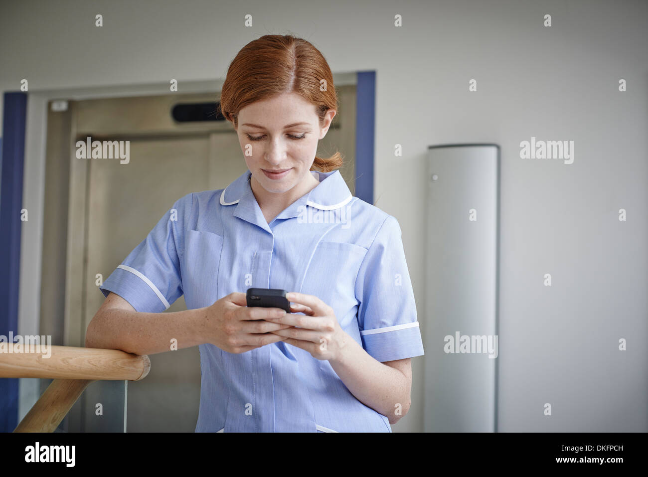 Krankenschwester, Blick auf Handy vor Krankenhaus Aufzug Stockfoto