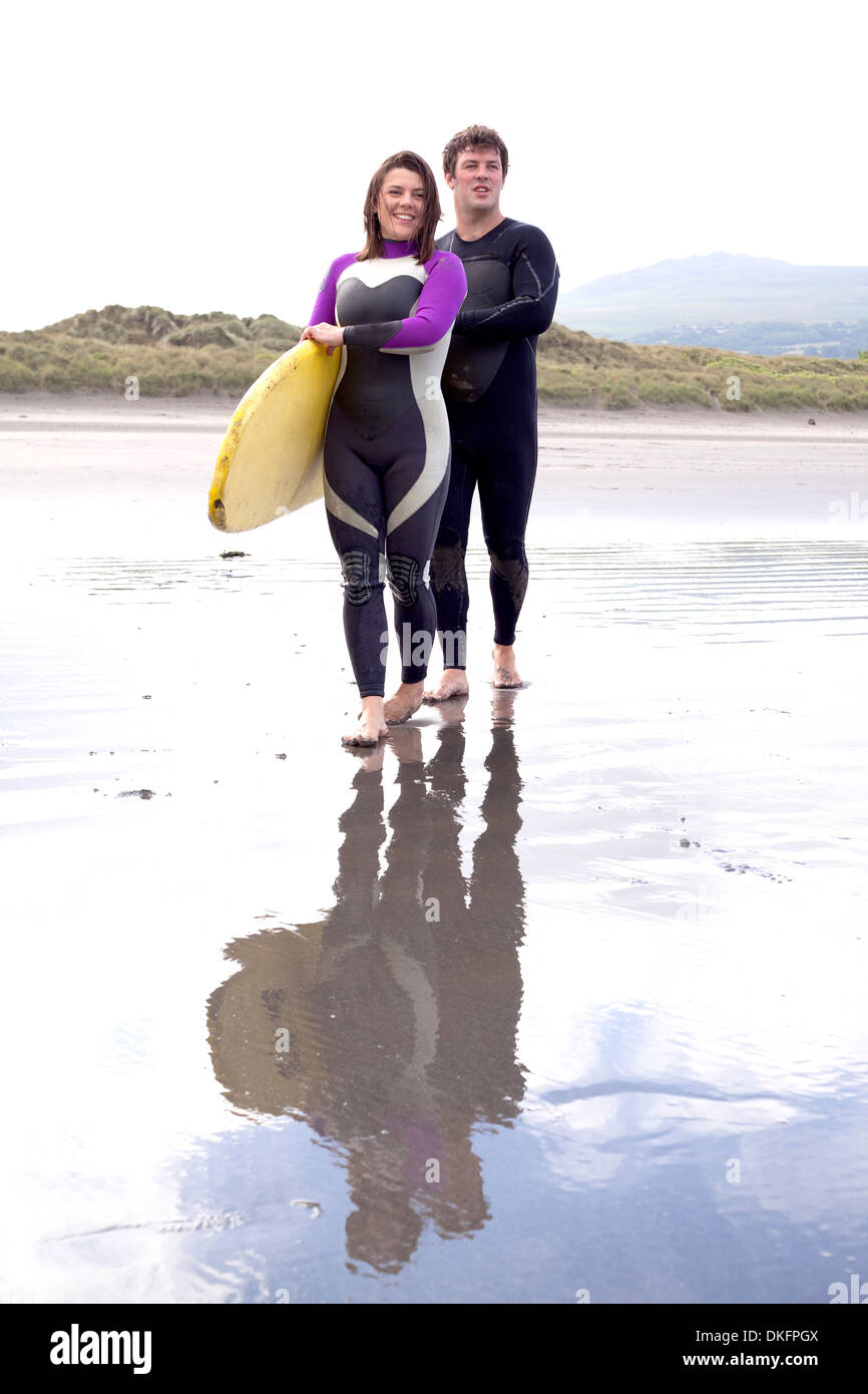 Porträt des Paares mit Surfbrett am Strand Stockfoto