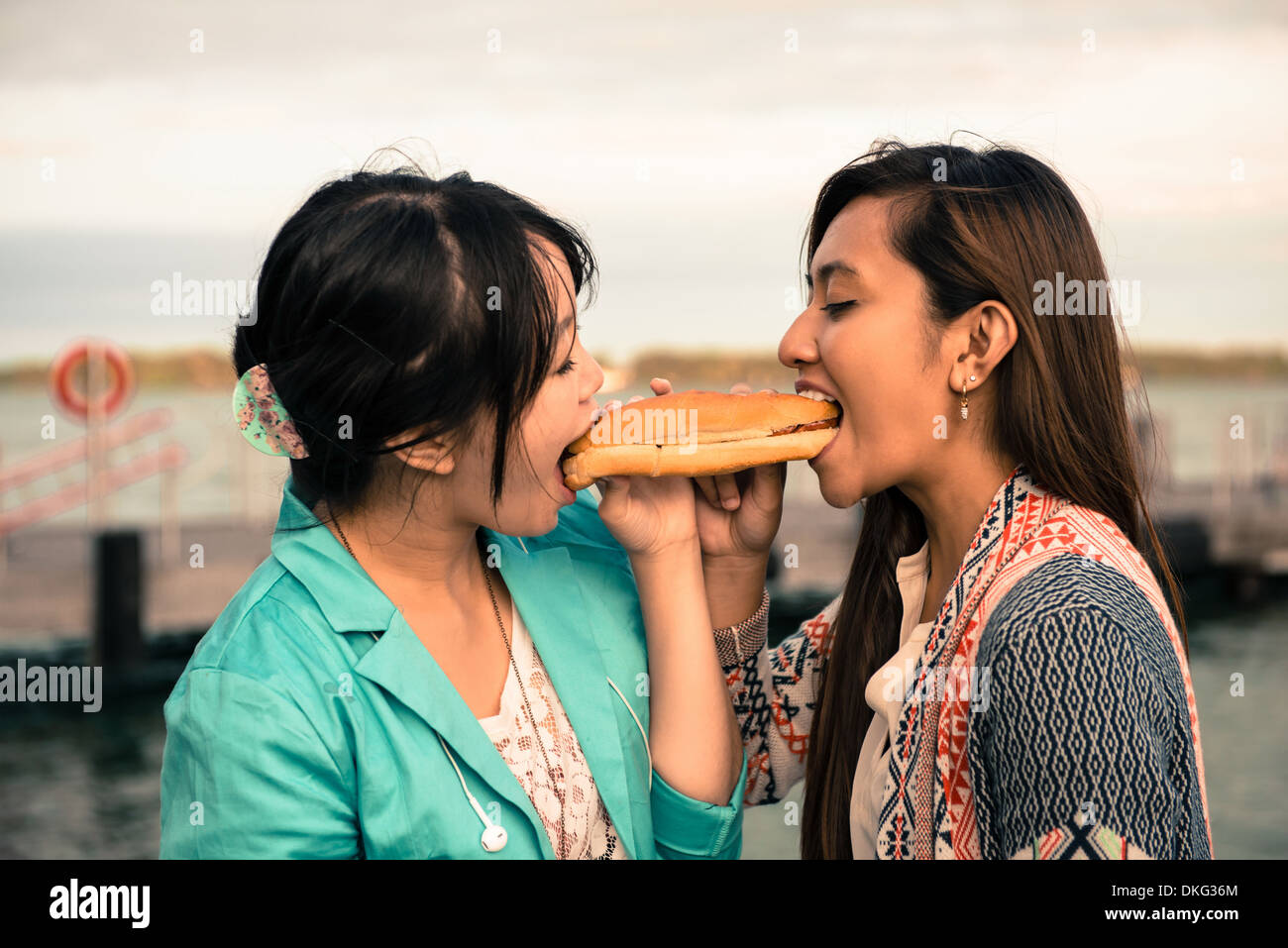 Junge Frauen beißen entgegengesetzte Enden des sandwich Stockfoto