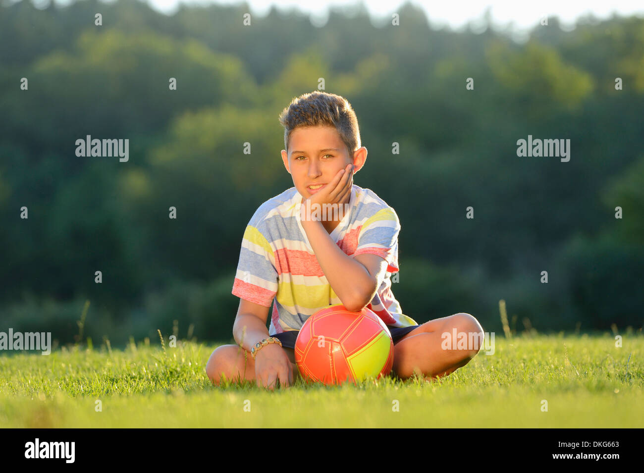 Teeange Junge sitzt mit Fußball auf der Wiese, Oberpfalz, Deutschland, Europa Stockfoto