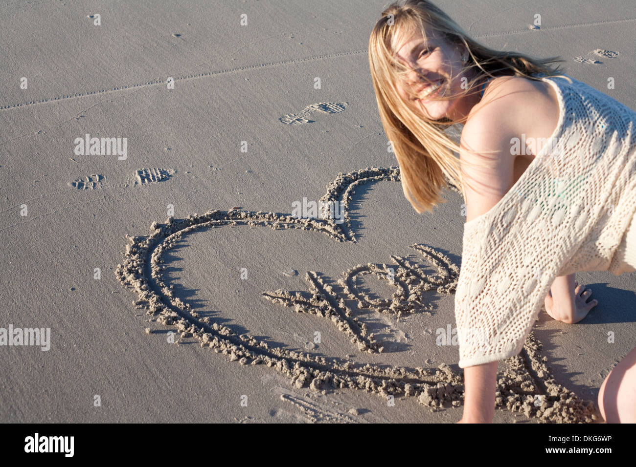 Lächelnde Frau schreiben Liebesbotschaft im Sand, Breezy Point, Queens, New York, USA Stockfoto