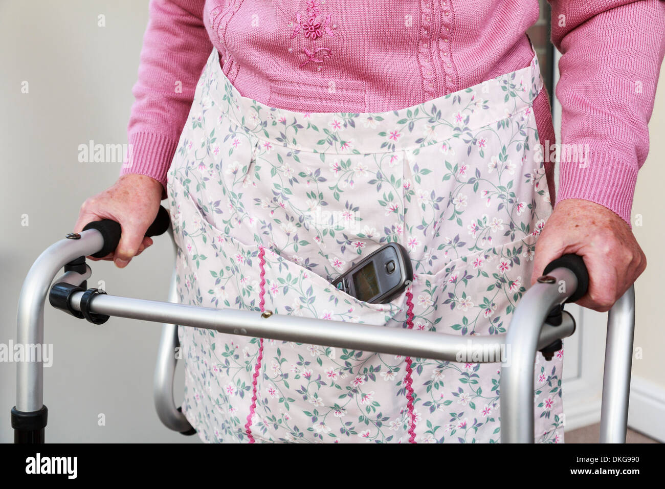 Ältere ältere Frau, die ein schnurloses Telefon Hörer in eine Schürze Tasche mit einem Walker für Unterstützung stehen. England, Großbritannien, Großbritannien Stockfoto
