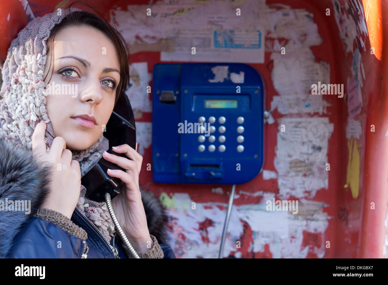 Nahaufnahme des Gesichts von einer attraktiven Frau in ein Kopftuch öffentlichen Telefon aus anrufen eine Telefonzelle stehen mit dem Empfänger zu ihrem Ohr. Stockfoto