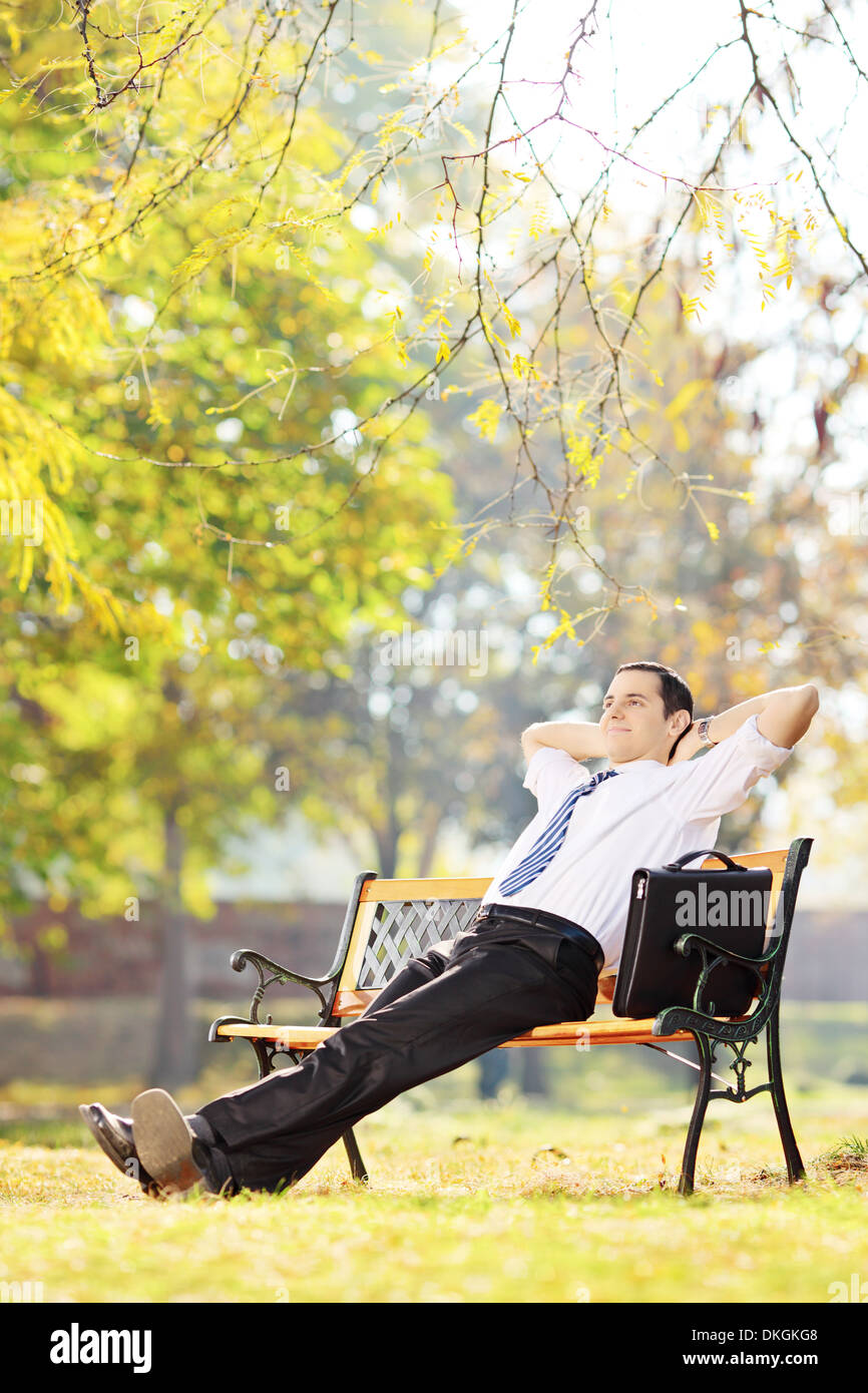 Junger Geschäftsmann sitzt auf einer Parkbank entspannend Stockfoto