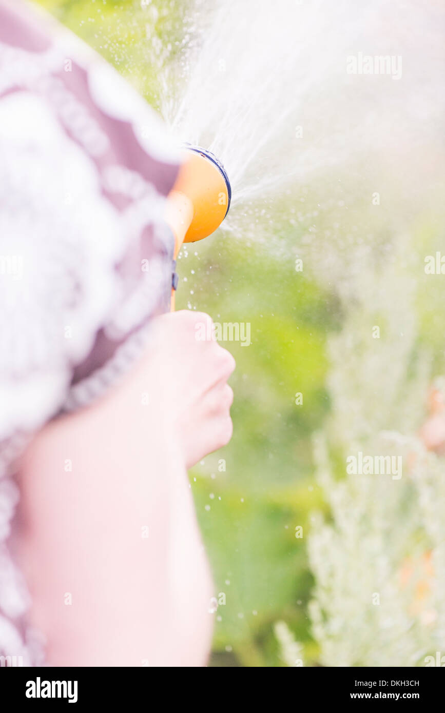 Rückansicht der Frau hält einen Garten Sprinkler, Bewässerung von Pflanzen hautnah Stockfoto