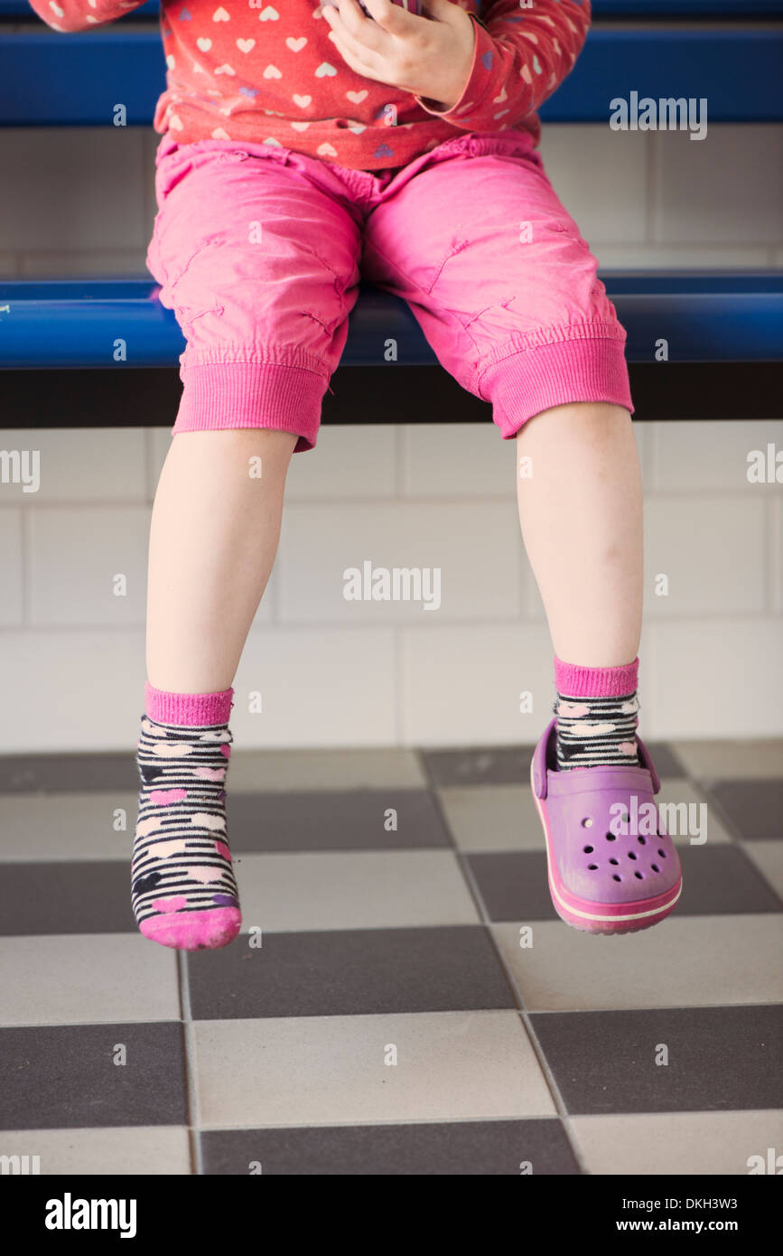 Junge Mädchen tragen einen Schuh allein auf einer Bank sitzend Stockfoto
