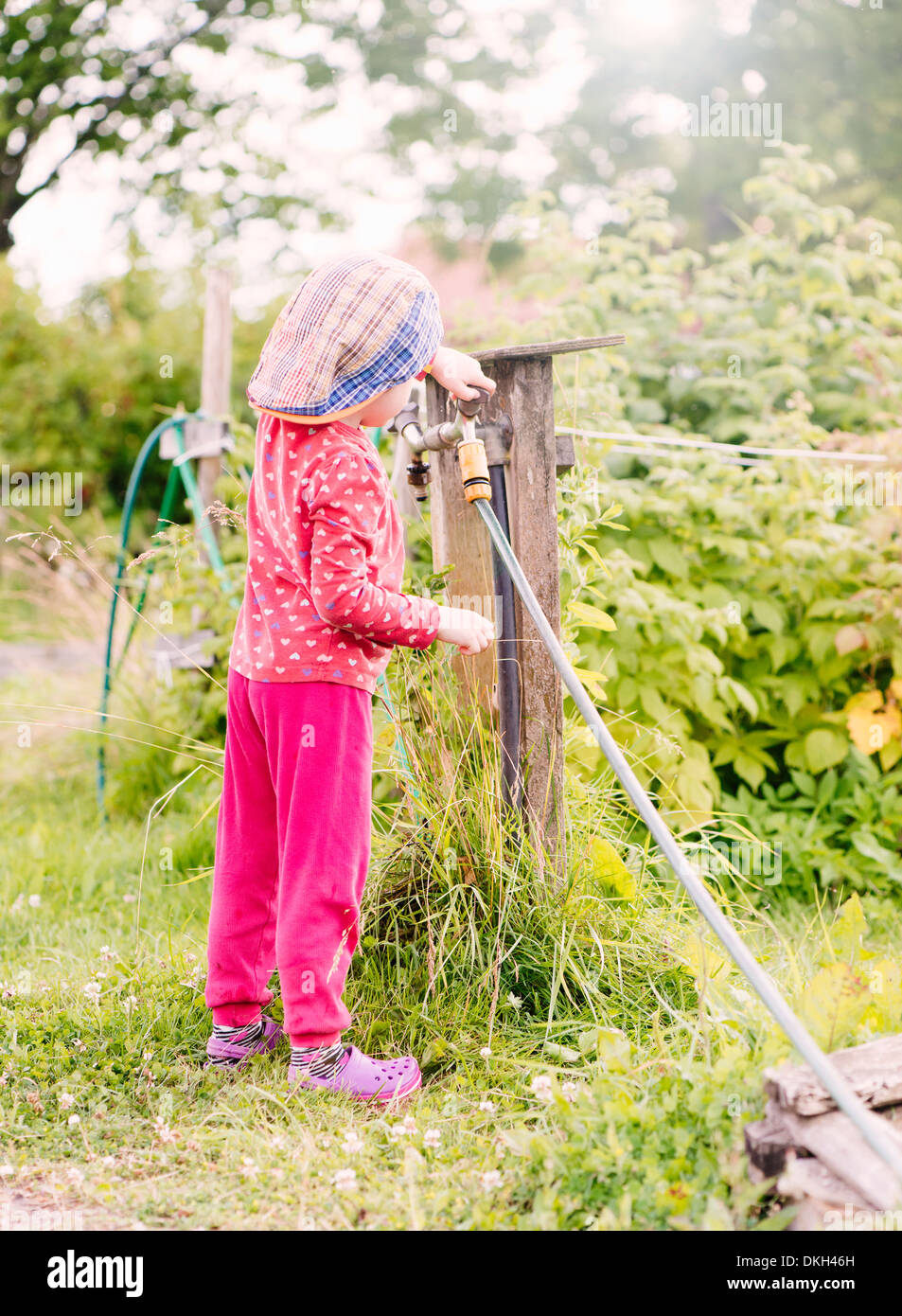 Seitenansicht des jungen Kindes stehen im Garten helfen mit dem Wasserschlauch Stockfoto