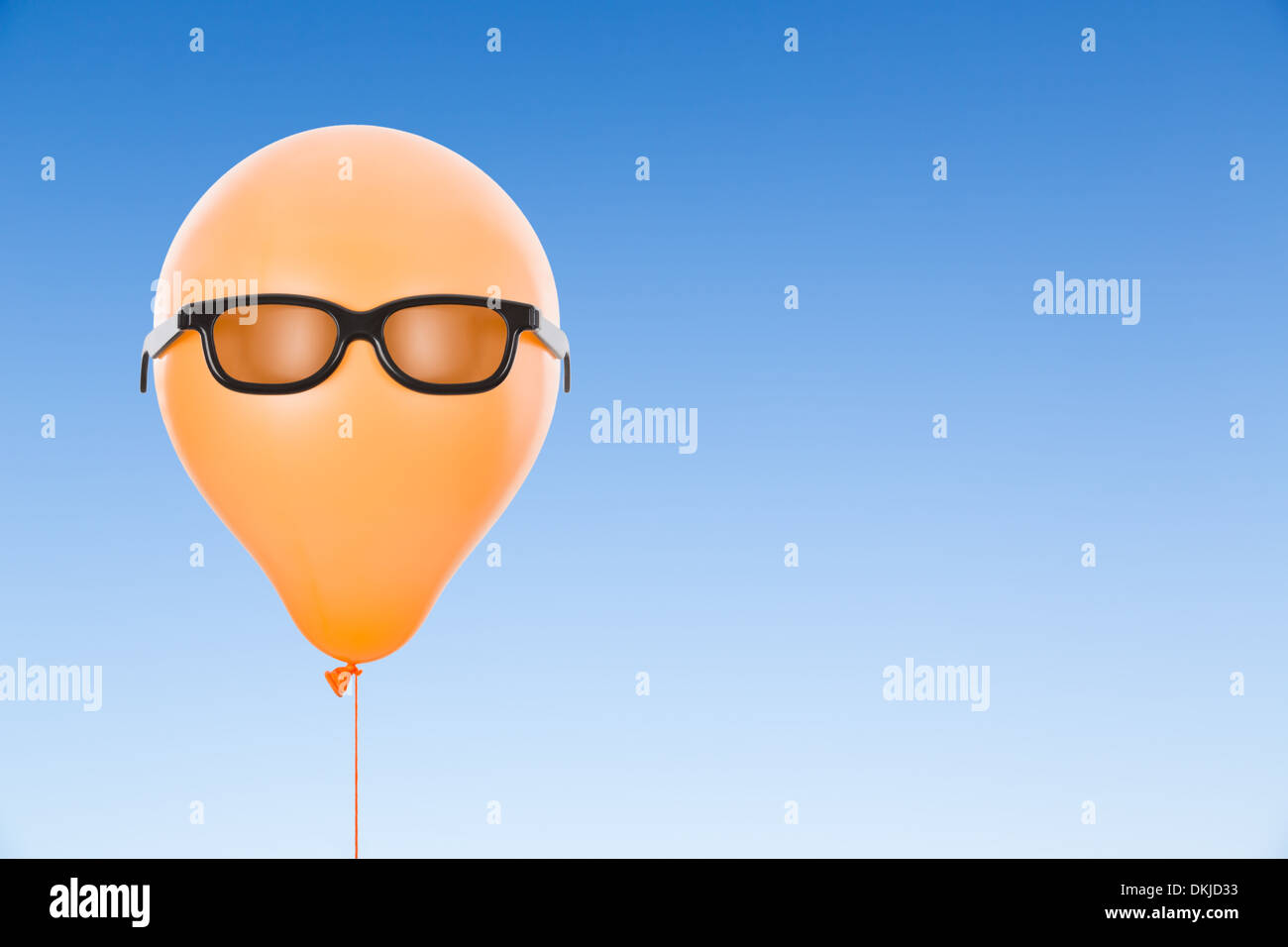 Orange-Ballon mit einer Sonnenbrille vor blauem Himmel mit Exemplar Stockfoto