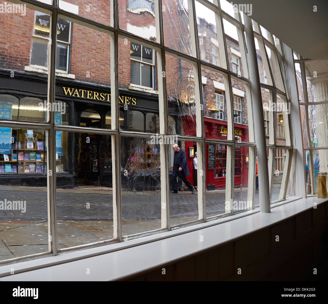 Ein Mann macht seinen Weg den Hügel hinauf in Durham, durch eine alte altmodische Schaufenster gesehen Stockfoto