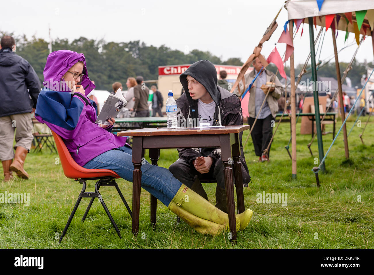 Ein paar saß an einem Tisch im Freien auf einem Musikfestival. Die junge Frau liest. Stockfoto