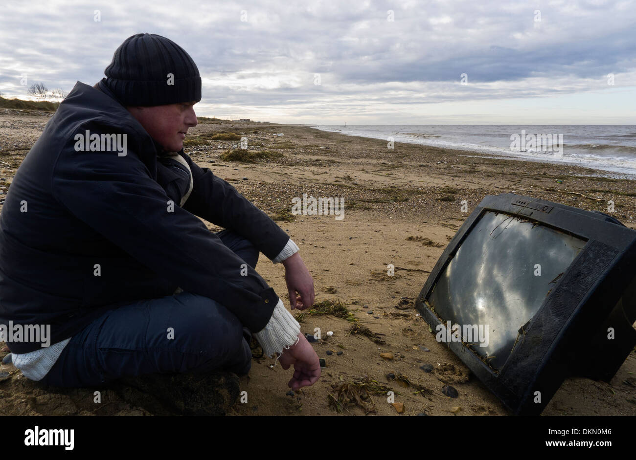 Mann beobachtet einen Fernseher an einen Strand gespült. Stockfoto