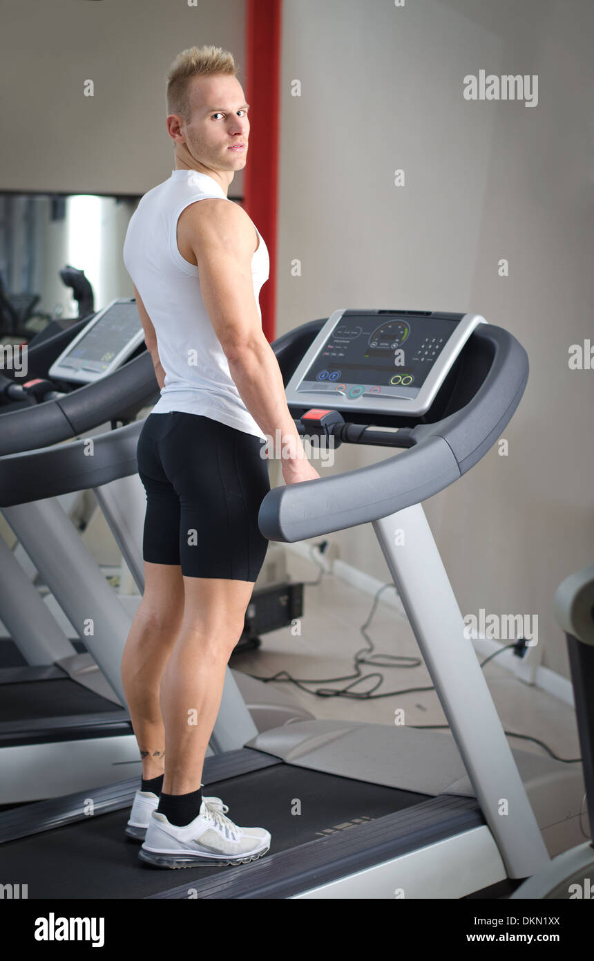 Blonde attraktive junge Mann auf Laufband, gesehen von hinten, Blick in die Kamera Stockfoto